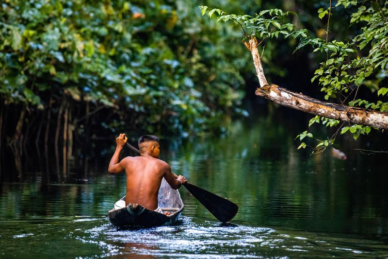 Native man sailing in AMazon river rainforest in handmade boat