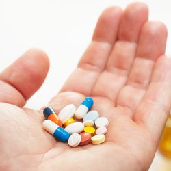 hand holding lots of different coloured and shaped pills with a bottle of alcohol and a glass in the background out of focus