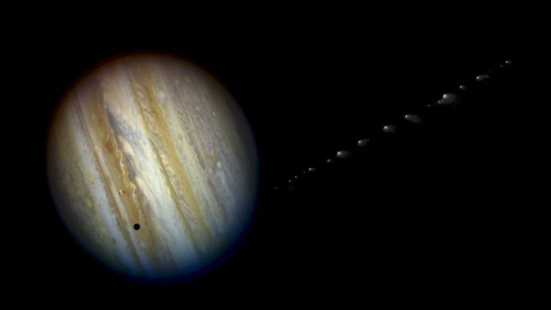 Jupiter is seen on its side with Io casting a small shadow on it. On the side small blurry fragements are seen trailing, the comet fragments approaching the planets