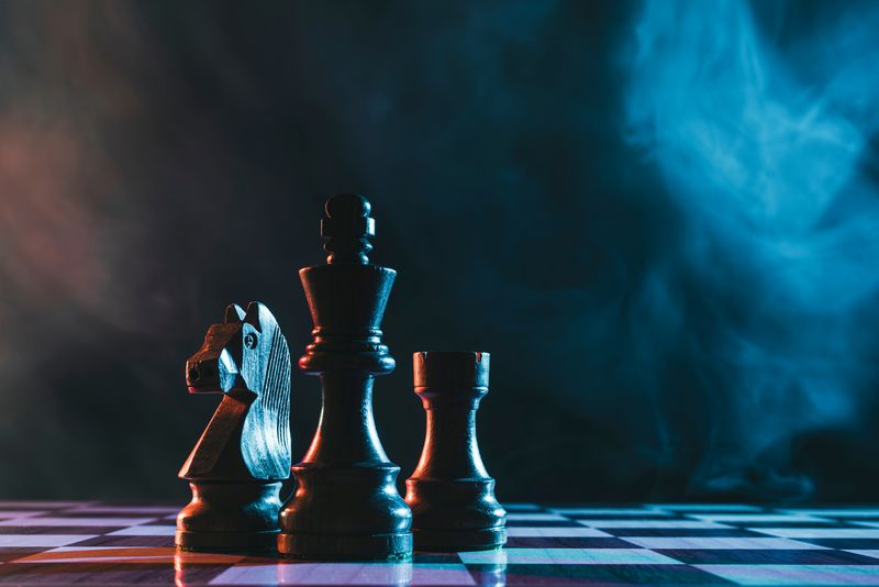Chess pieces on a blue and pink-lit chess board, smoke in the background