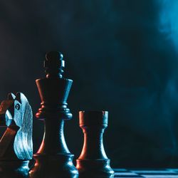 Chess pieces on a blue and pink-lit chess board, smoke in the background