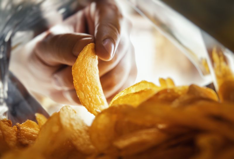Hand takes out potato chips, from inside the package