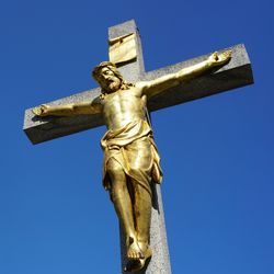 A gold Christ on a Christian Cross against a blue sky background 