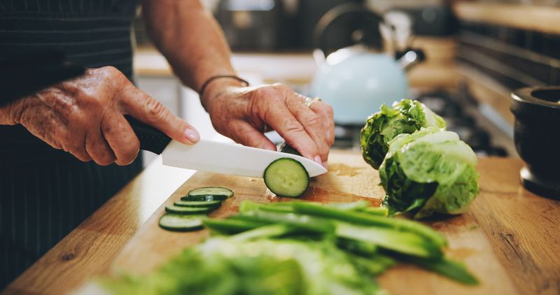 close up photograph of hands chopping up a cucumber on a wooden cutting board