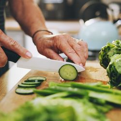 close up photograph of hands chopping up a cucumber on a wooden cutting board