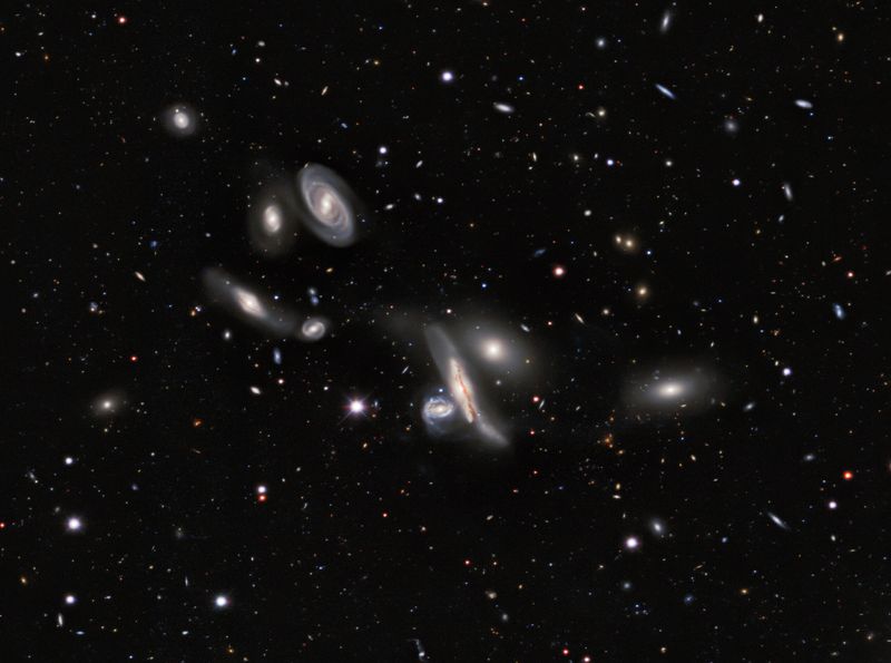 seven galaxies are seen at the center of the image some are spirals are elliptical. the background is filled with smaller dots of light, galaxies that are located further away.