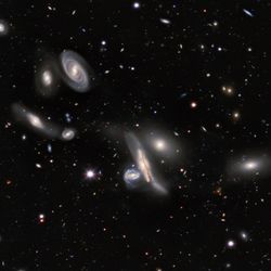 seven galaxies are seen at the center of the image some are spirals are elliptical. the background is filled with smaller dots of light, galaxies that are located further away.