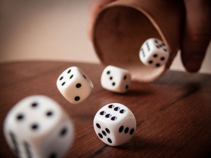 Five dice being thrown out of a cup onto a table