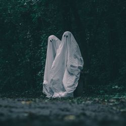 Two people dressed as ghosts with sheets and eye cut outs in a dark wood