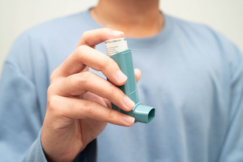 close up of person's hand holding blue asthma inhaler