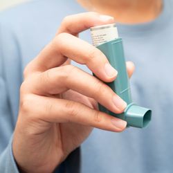 close up of person's hand holding blue asthma inhaler