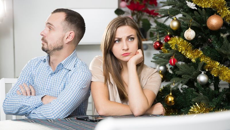 Man and woman looking grumpy next to a christmas tree
