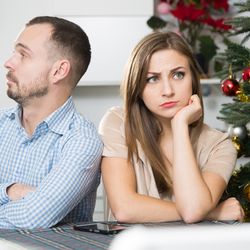 Man and woman looking grumpy next to a christmas tree