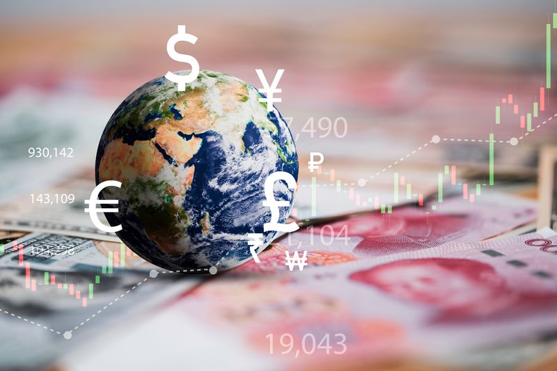 globe on a table covered with bank notes, with numbers, currency symbols and graphs to indicate the stock market overlaid on top in white, green and red