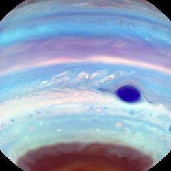The band and clouds of jupiter are visible in this image. the great red spot is starkingly clear in a dark color. The souther pole looks dimmer covered in this haze and among the haze a dark patch where the oval is