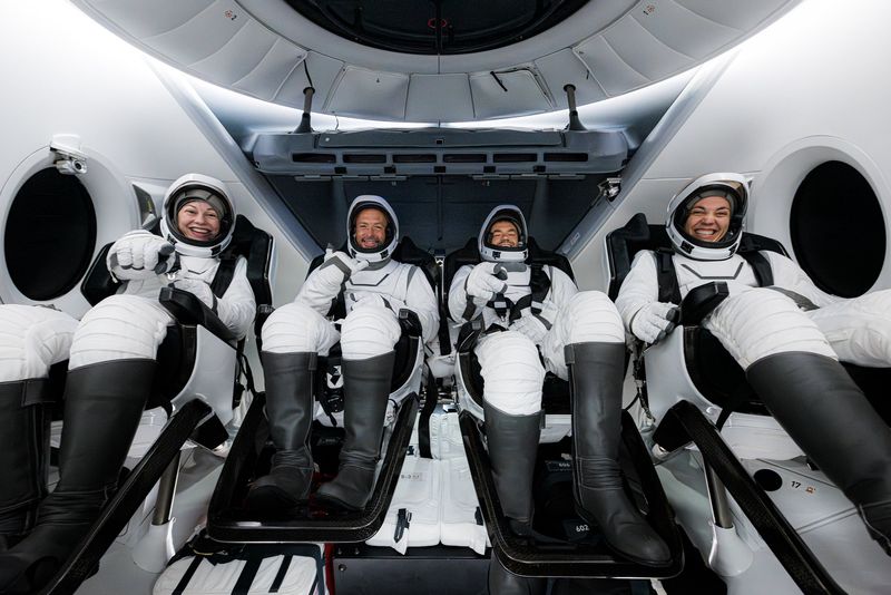 the four astronauts are seen in the capsule smiling and seated