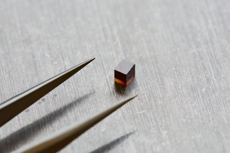 the tip of a pair of tweezer and next to them a small purple cube, the diamond in question