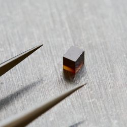 the tip of a pair of tweezer and next to them a small purple cube, the diamond in question