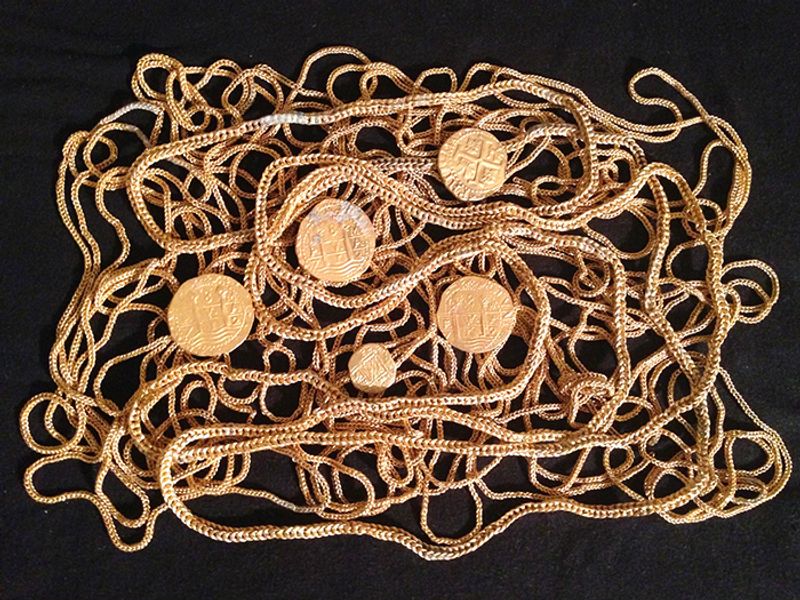 The photo shows five of the now recovered gold coins positioned on a mess of coiled gold chains as a form of display, set against a black background. 