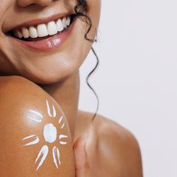 a woman showing a tanned shoulder with a sun drawn in sunscreen on it
