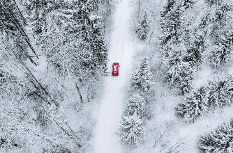 Aerial top view of snow covered forest with winter road and red car. Drone photography landscape.