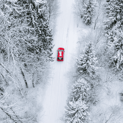 Aerial top view of snow covered forest with winter road and red car. Drone photography landscape.