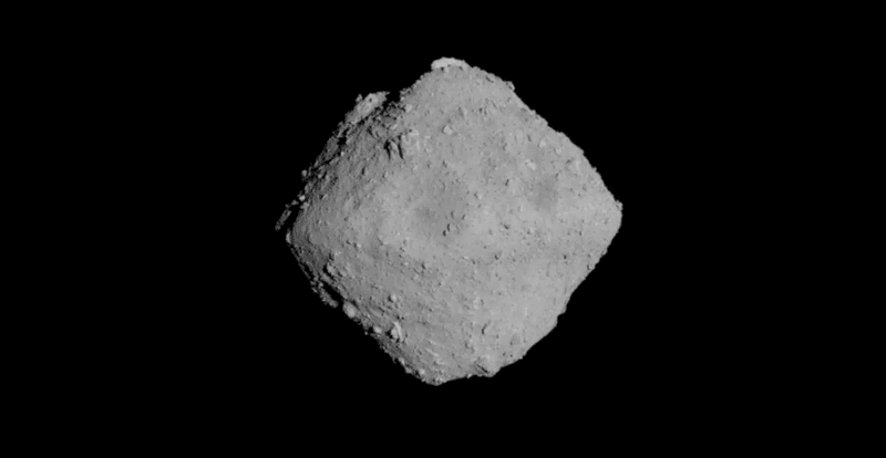 the asteroid is a grey rhombus against the black of space. it is has a rough surface with several boulders visible on it.