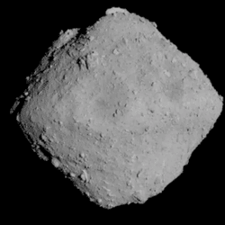the asteroid is a grey rhombus against the black of space. it is has a rough surface with several boulders visible on it.
