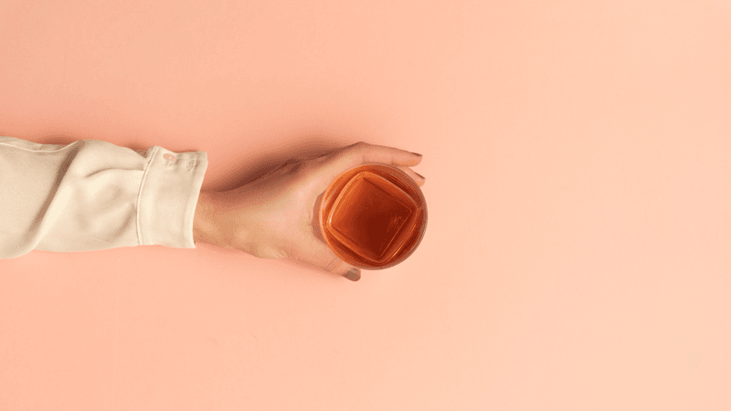 top-down view of whisky in a tumbler, a hand is reaching out to grab it