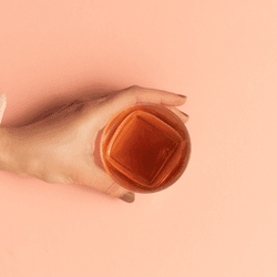 top-down view of whisky in a tumbler, a hand is reaching out to grab it