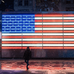 The silhouette of a person stands in front of an illuminated American flag in Times Square, New York City, during a snowstorm.